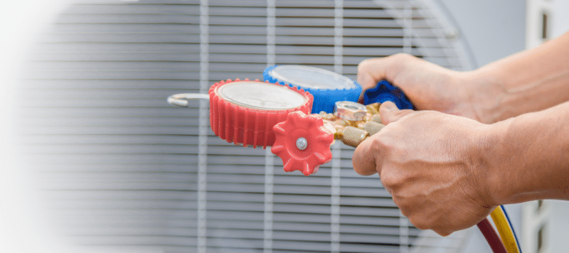 A close-up of a person adjusting red and blue HVAC pressure gauges near an air conditioning unit